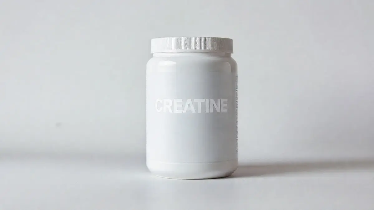 Pote de creatina em pó totalmente sem marca sobre uma superfície elegante, ilustrando os benefícios do suplemento para o corpo feminino.