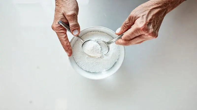 Mãos de uma pessoa idosa preparando a dosagem correta de creatina em pó em um copo de água em uma cozinha limpa.