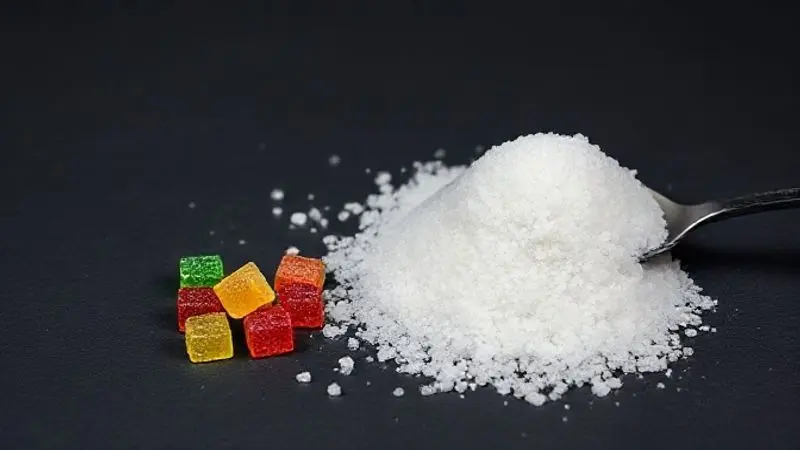 Imagem conceitual alertando sobre o excesso de açúcar na creatina em goma, mostrando gomas ao lado de uma colher transbordando de açúcar.